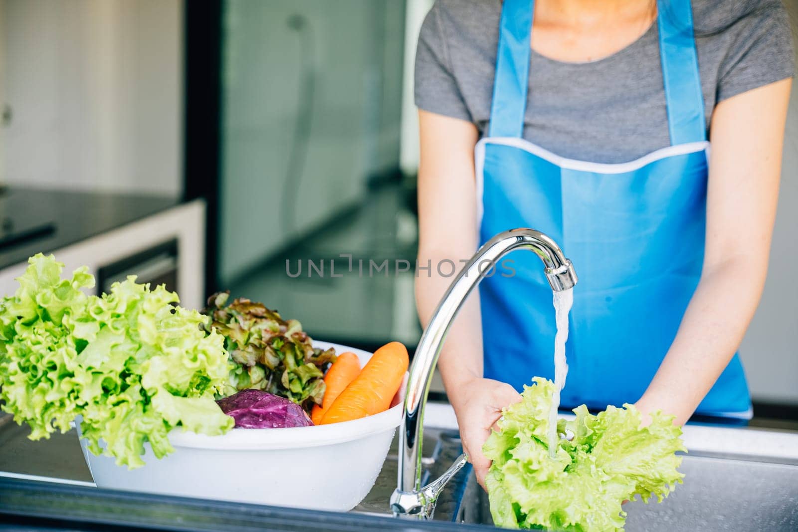 A joyful woman washes and prepares fresh vegetables in her kitchen sink for a vibrant salad enjoying her vegetarian lifestyle with healthy clean eating habits at home.
