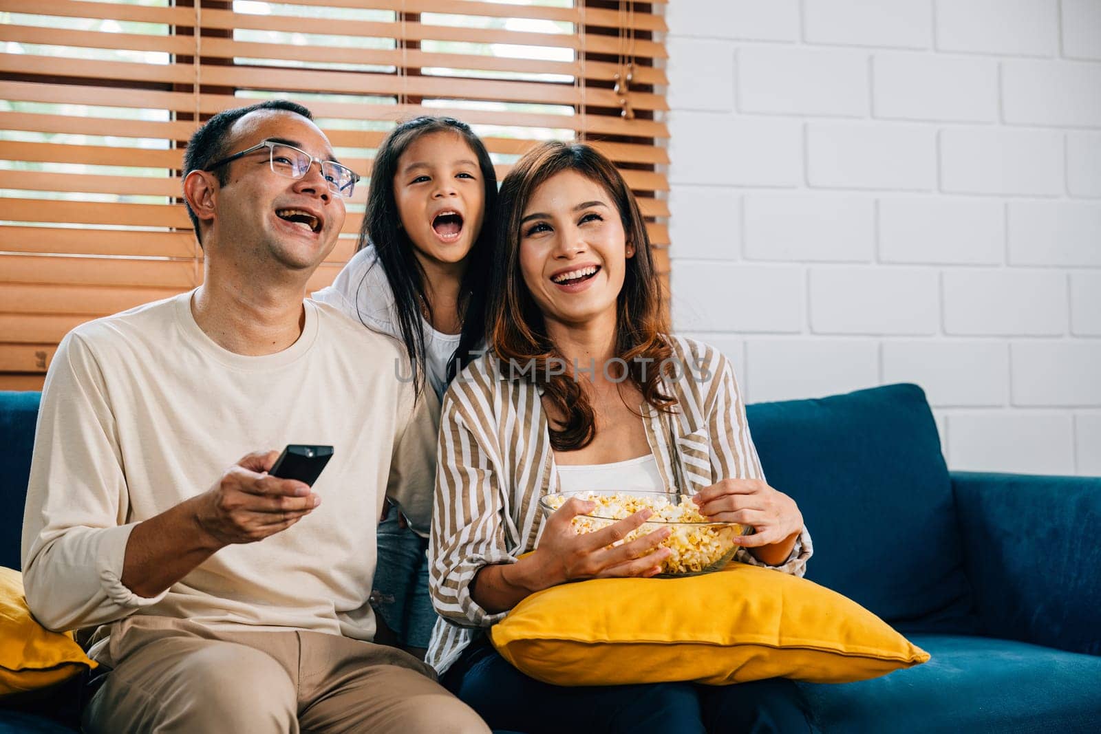 In their cozy house smiling family gathers on sofa for video time watching TV with popcorn. father mother son daughter and schoolgirl share laughter happiness and enjoyment fostering togetherness.