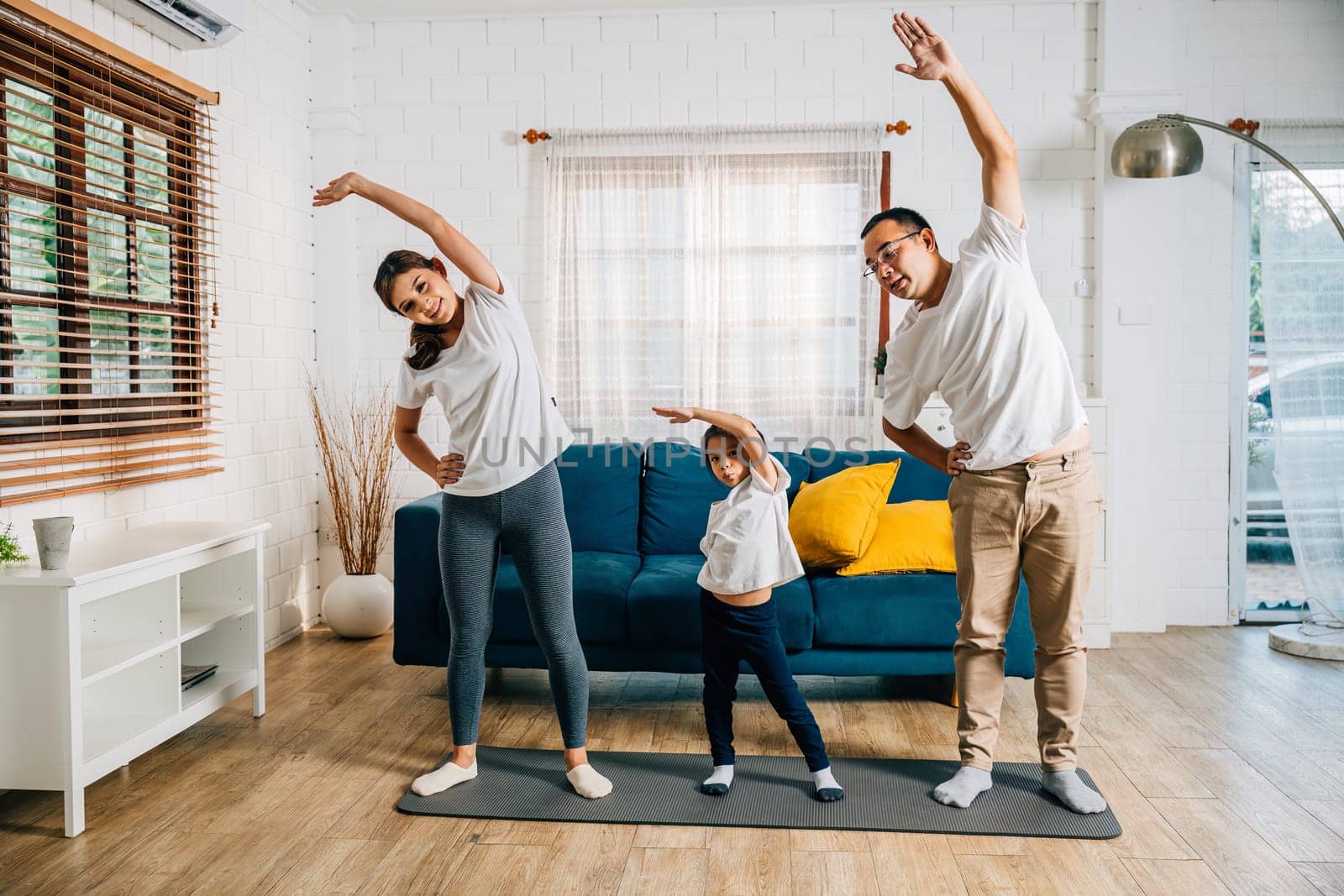 A family of three Asian parents and their daughter focus on yoga and fitness training at home fostering health happiness and education.