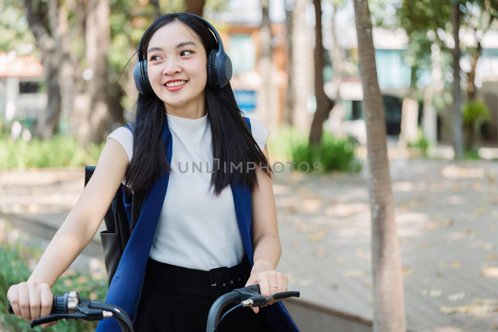 Asian young businesswoman bike to work for eco friendly green energy and listen music with headphone while commuting in city. Eco friendly by itchaznong