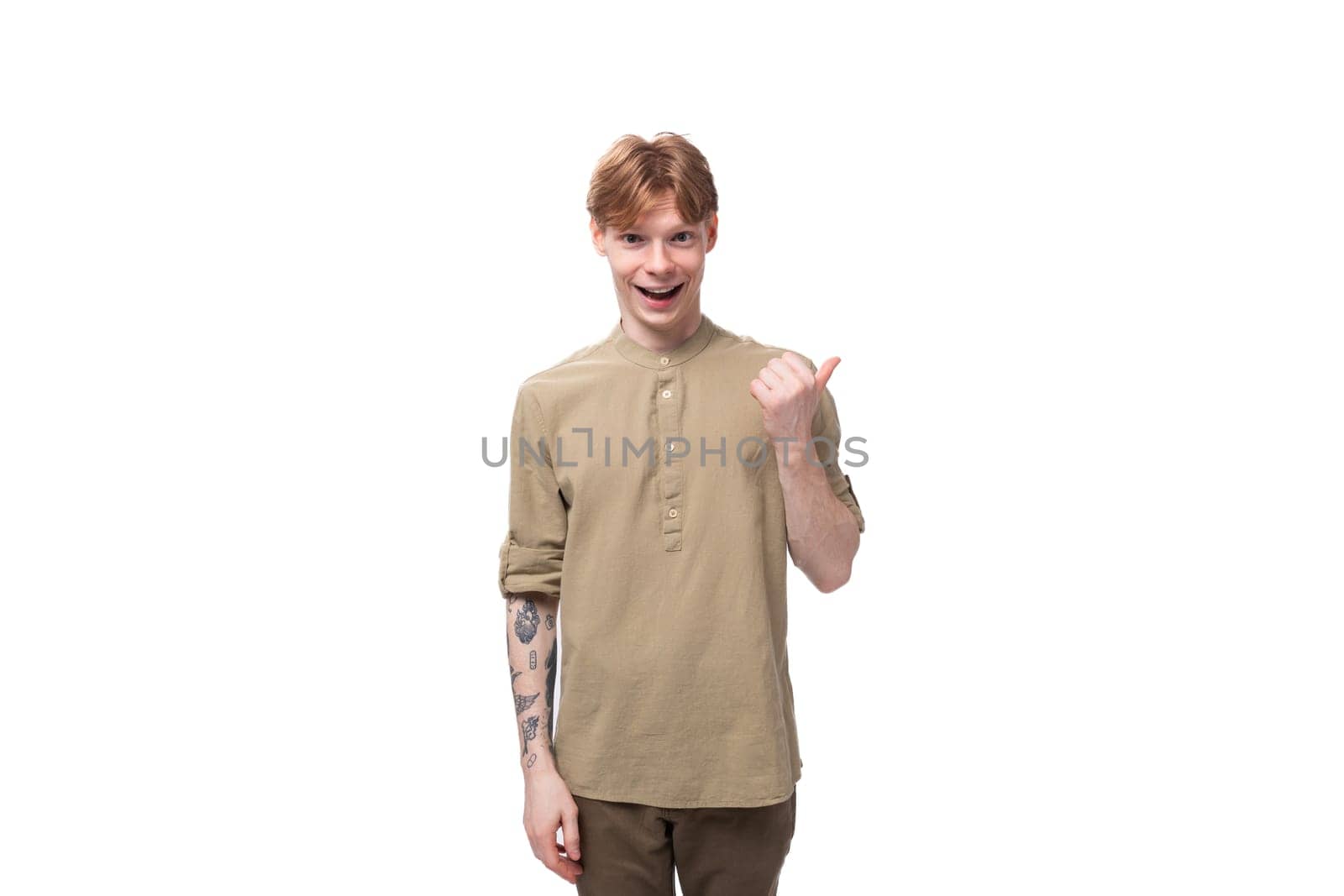 young red-haired man in a beige shirt points his finger to the side on a white background.