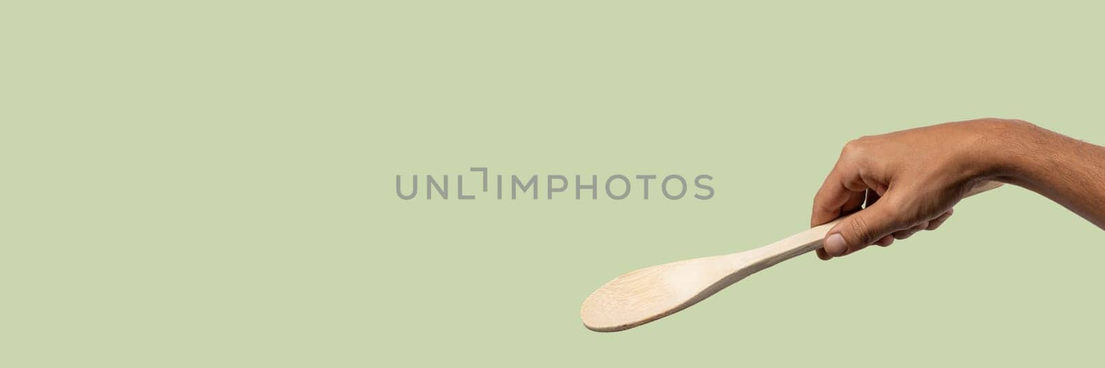 Black male hand holding a wooden cooking spoon isolated on light green background. High quality photo