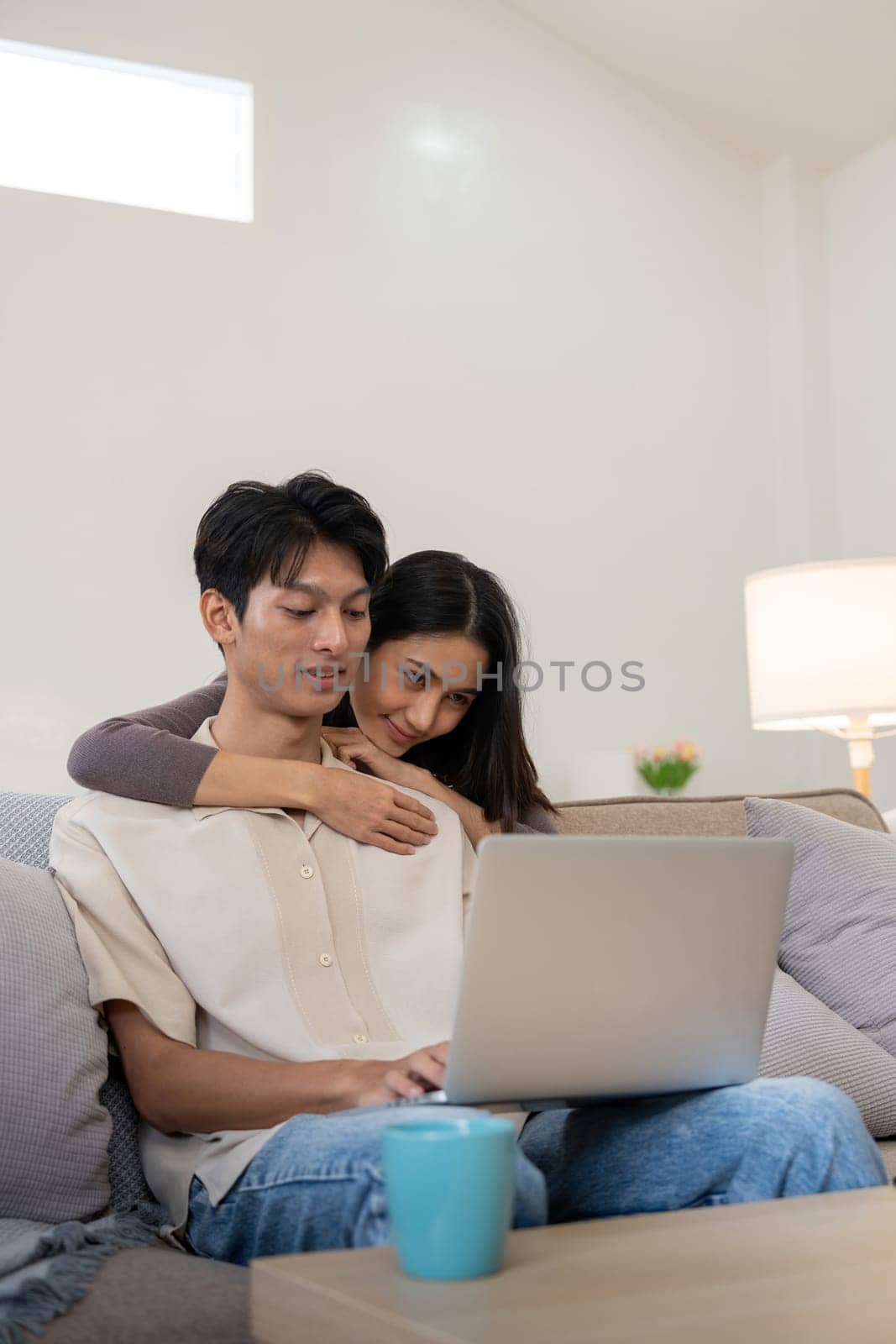 Happy asian couple using laptop sit relax on sofa doing ecommerce shopping online on website at home by nateemee