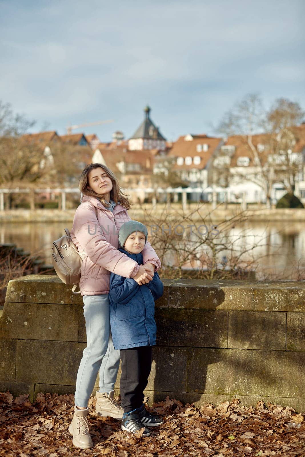Riverside Family Harmony: Mother, 30 Years Old, and Son - Beautiful 8-Year-Old Boy, Standing by Neckar River and Historic Half-Timbered Town, Bietigheim-Bissingen, Germany, Autumn by Andrii_Ko