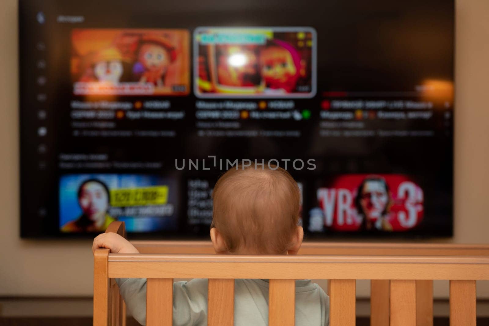 The baby watches a large TV from a crib. Concept of knowledge of the world.
