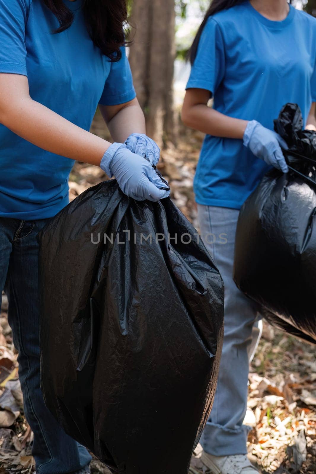 Up close, a group of Asian volunteers collects trash in plastic bags and cleans areas in the forest to preserve the natural ecosystem. by wichayada