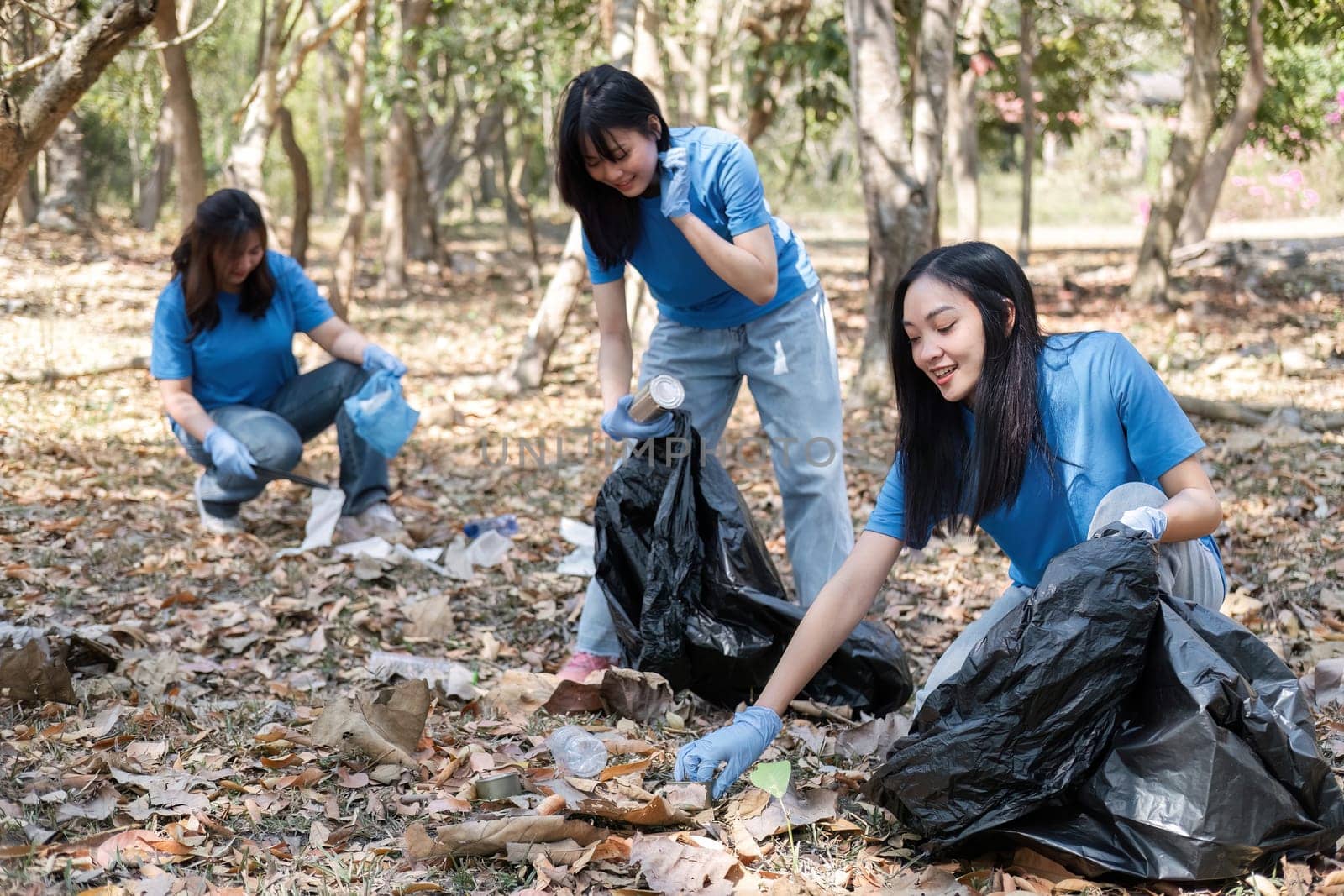 A group of Asian volunteers collects trash in plastic bags and cleaning areas in the forest to preserve the natural ecosystem..