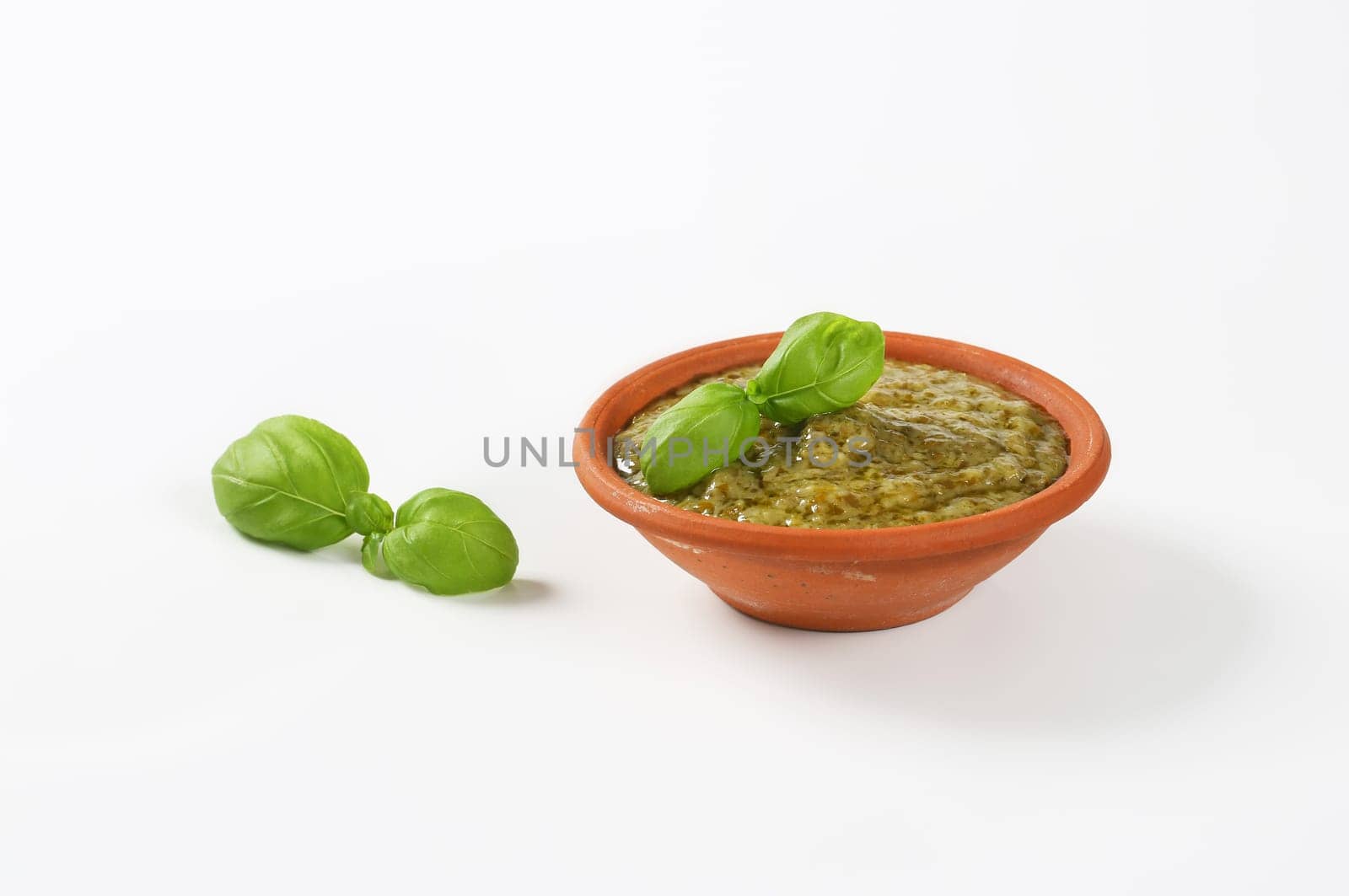 Basil pesto in terracotta bowl on white background