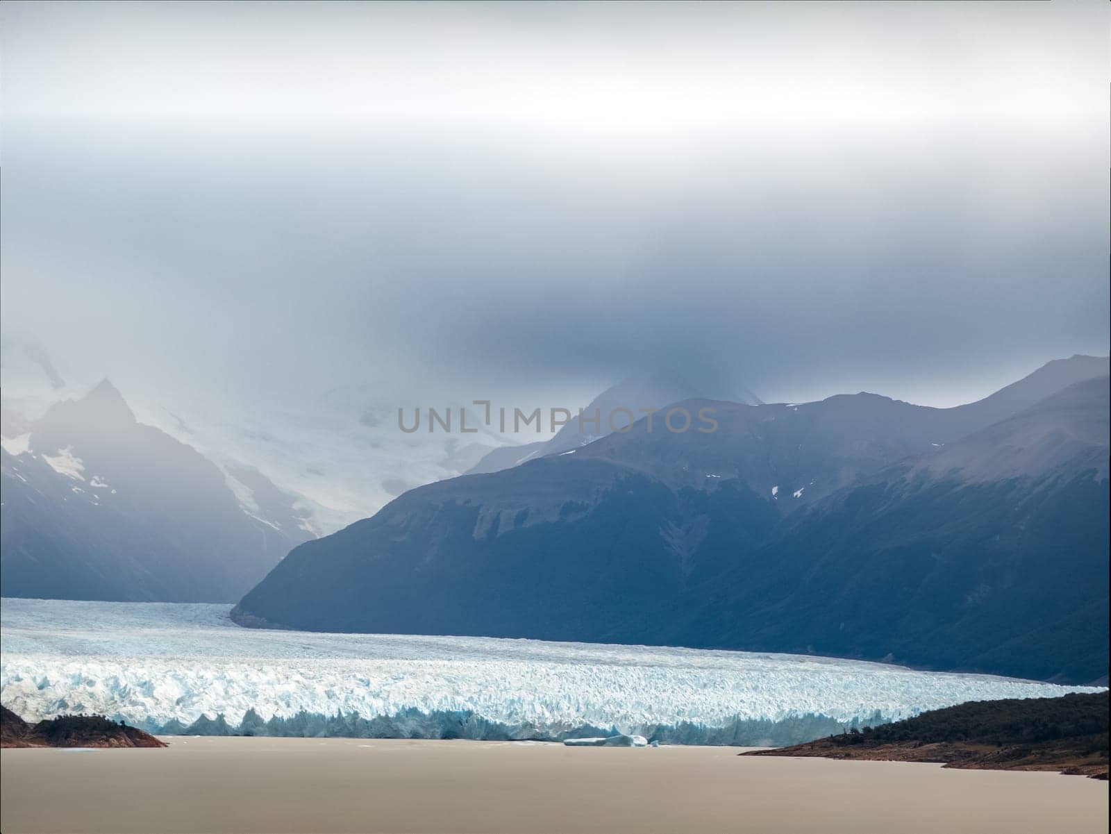 Glacier and mountains under dramatic cloudy sky.
