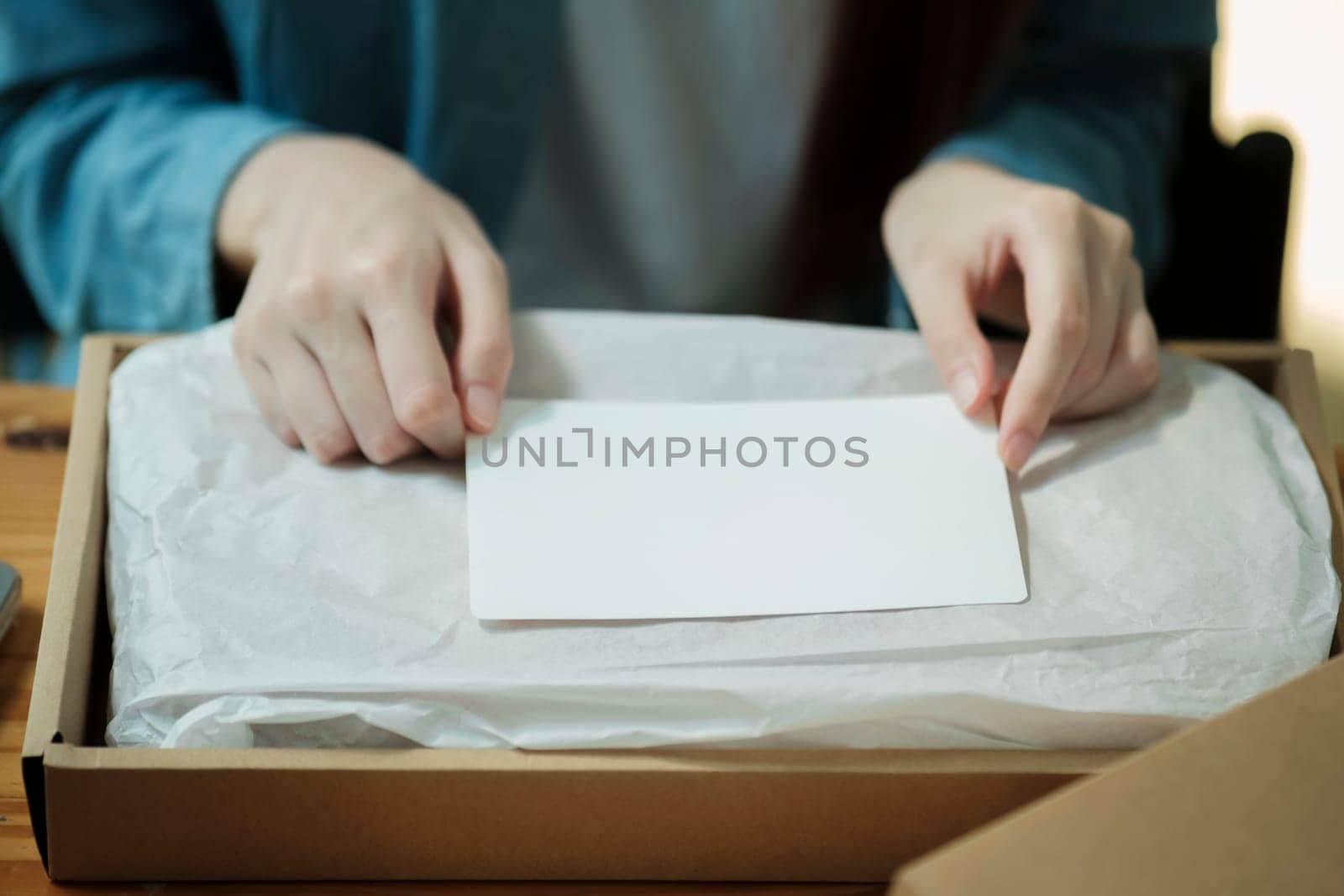 Person preparing a package with a blank card for a custom message. Product packaging and personalization concept. Design for e-commerce, gift wrapping services.
