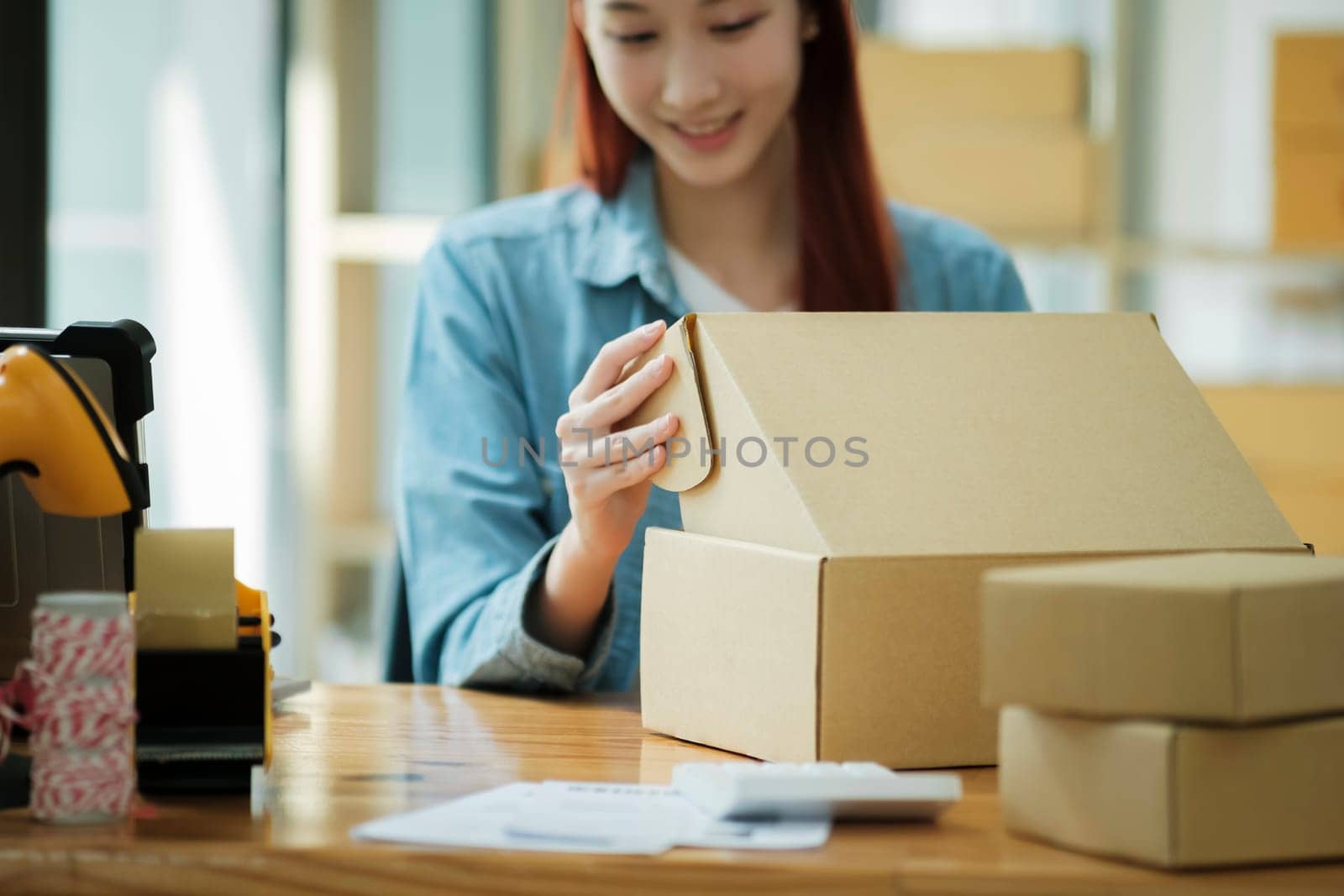 Smiling female entrepreneur packing clothing items for shipping in her startup workshop.