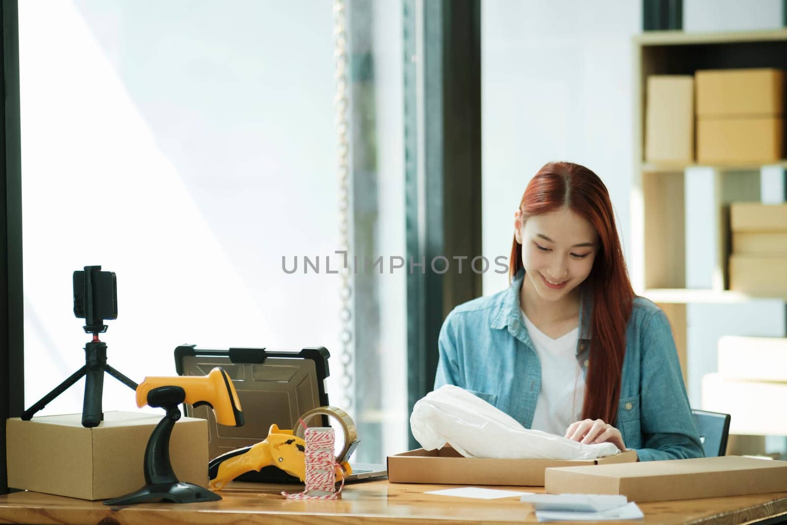 Smiling female entrepreneur packing clothing items for shipping in her startup workshop.