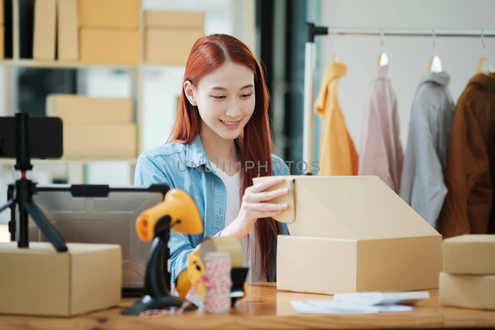 Smiling female entrepreneur packing clothing items for shipping in her startup workshop.