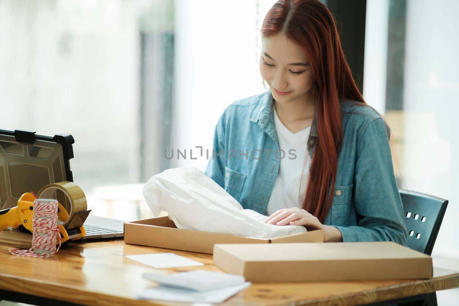 Smiling female entrepreneur packing clothing items for shipping in her startup workshop.