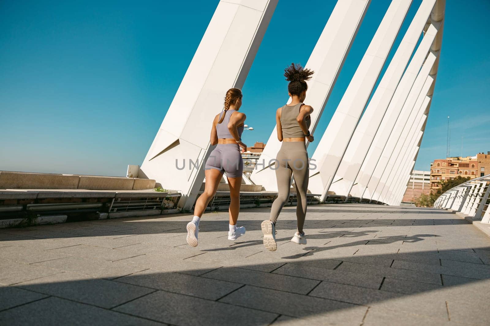 Two young women in sportswear are running on modern buildings background. Active lifestyle concept