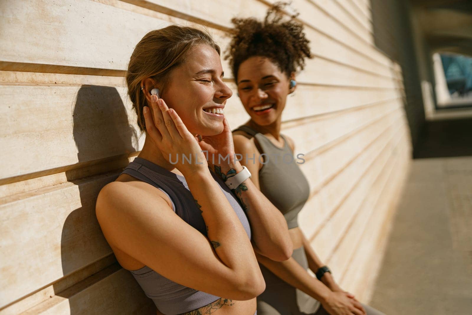 Two young female sportswomen have a rest after morning jogging outdoors and listen music