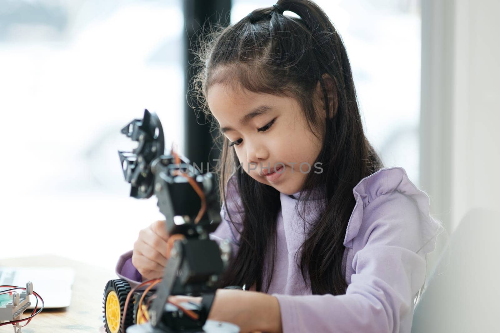 Asian girl concentrating on building a robot, embodying STEM education.