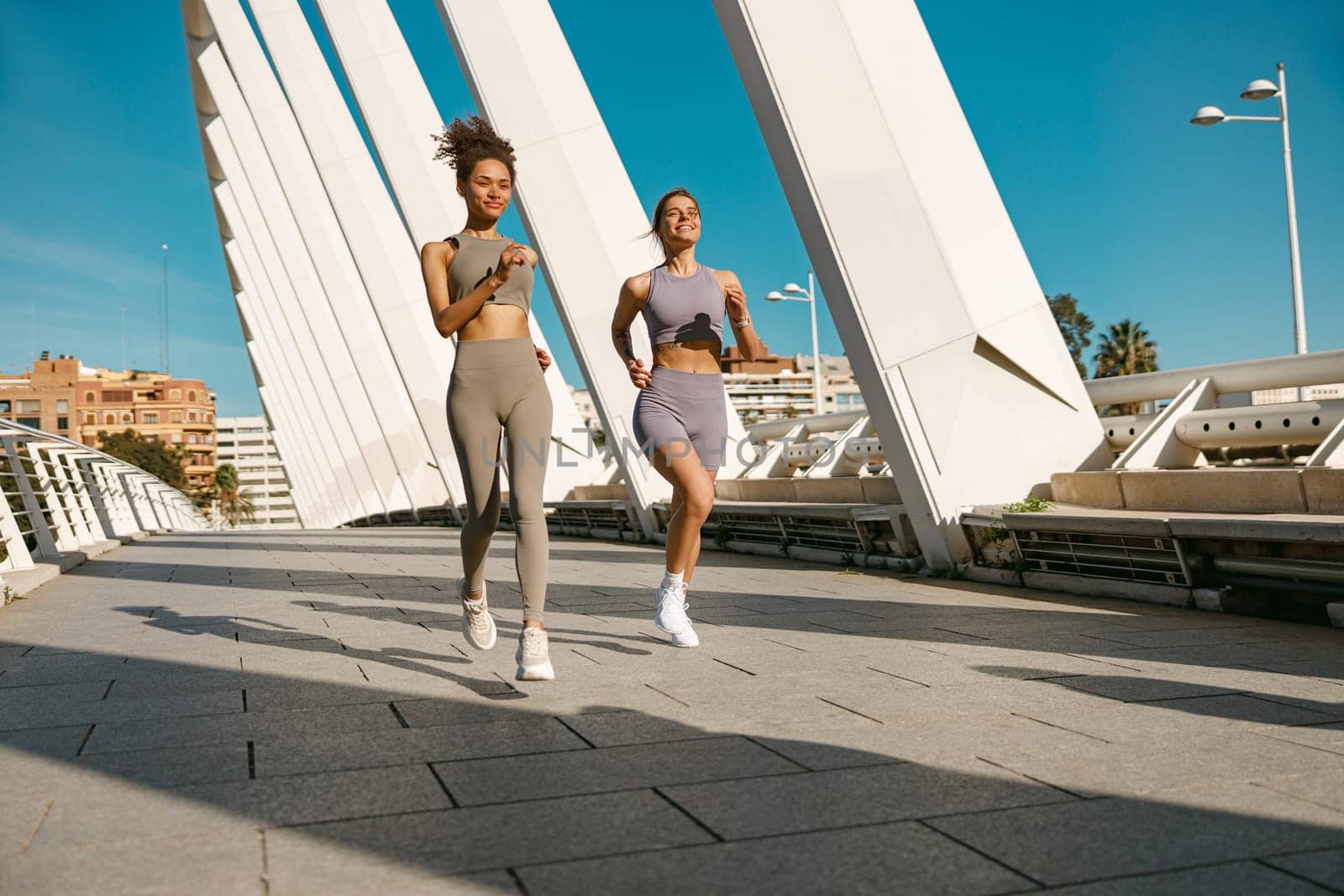 Two active women athlete running side by side along an outdoor track on modern buildings background by Yaroslav_astakhov