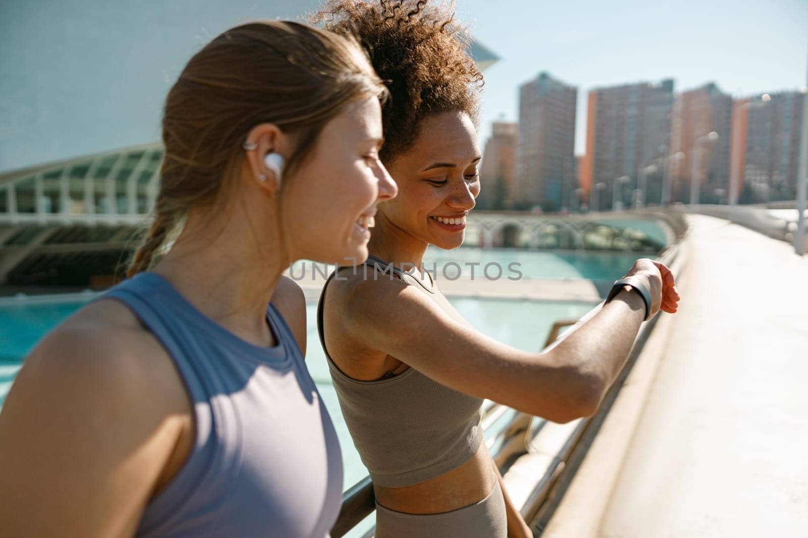 Smiling woman with female friend looking on smartwatch before exercising standing outdoors by Yaroslav_astakhov