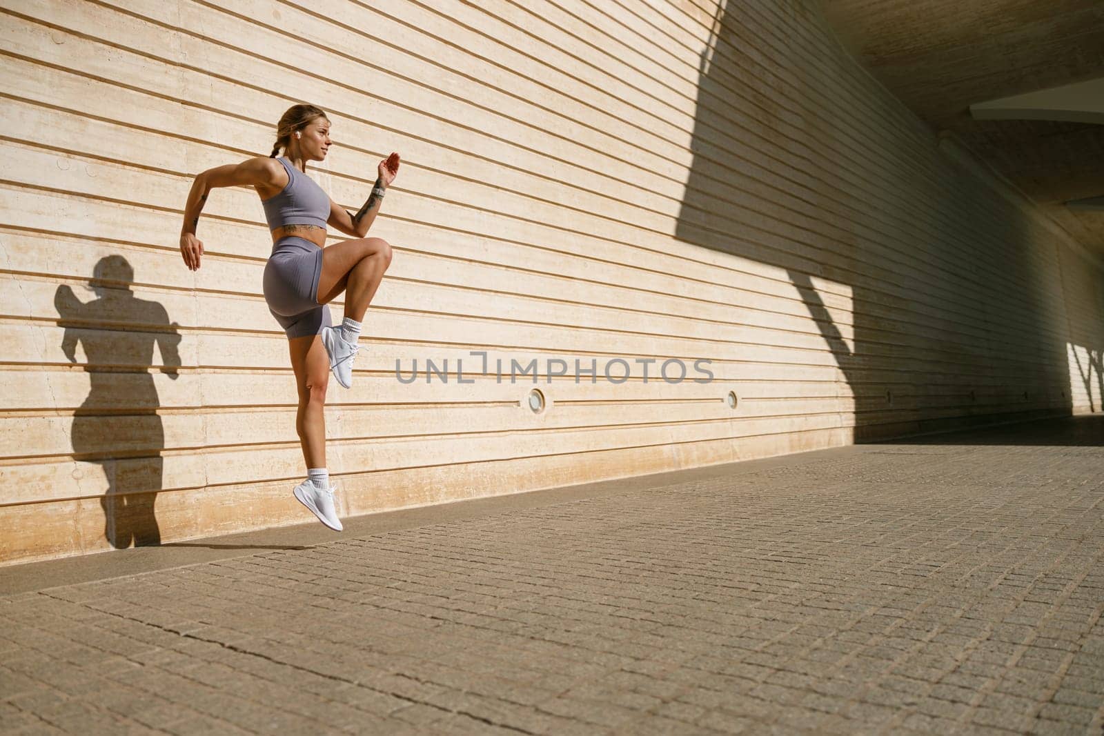 Young fit woman in sportswear leaping in the air with wall backdrop outdoors. High quality photo