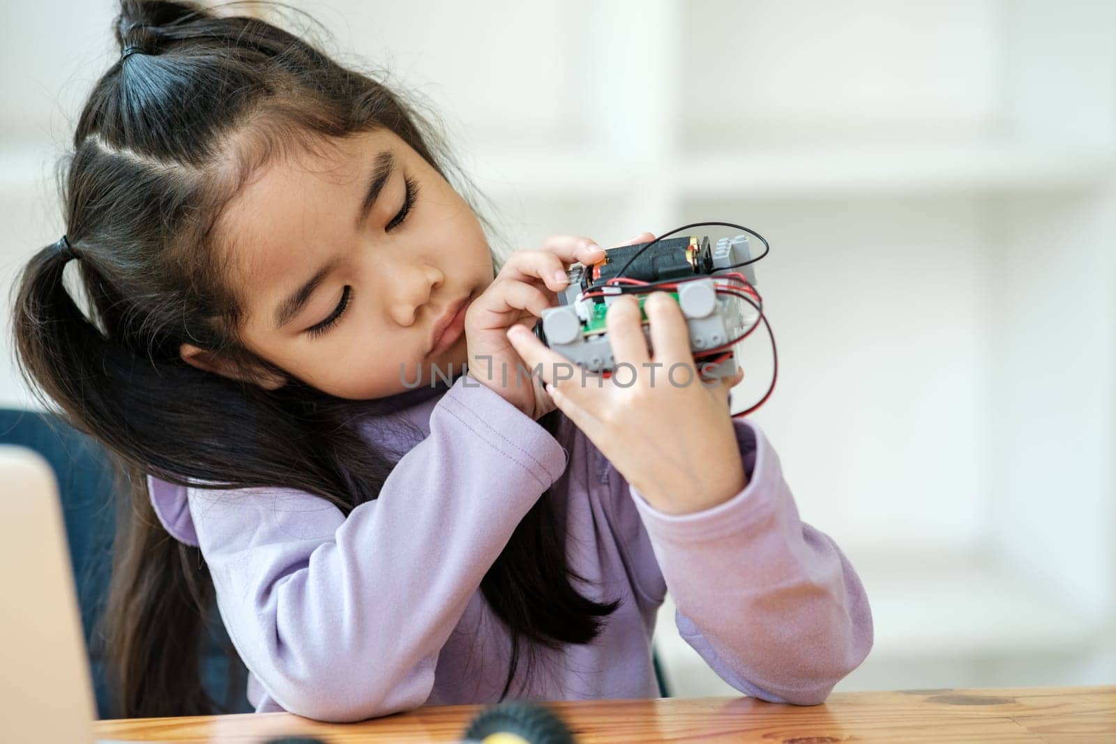 Asian girl concentrating on building a robot, embodying STEM education.