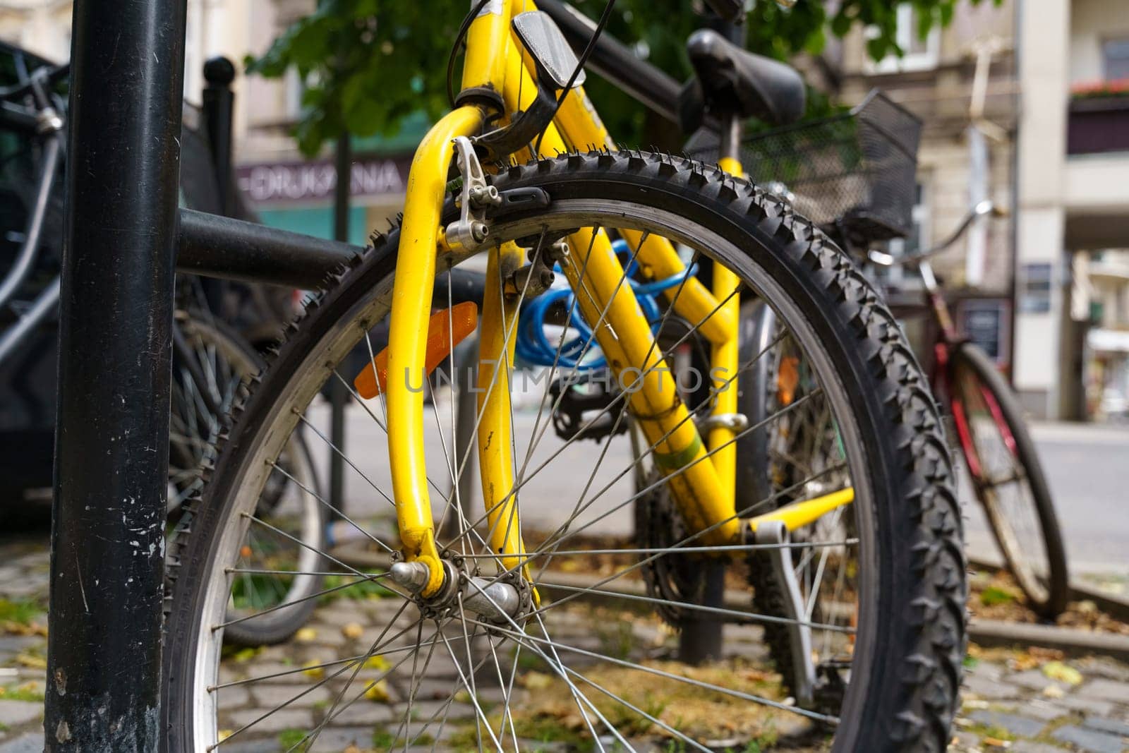 A vibrant yellow bicycle is parked neatly next to a black pole in an urban setting.