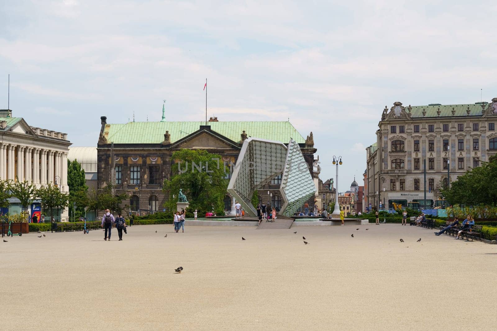 Poznan, Poland - June 18, 2023: Liberty Fountain. A contemporary art sculpture serves as a focal point in a bustling city square, surrounded by visitors and historic architecture under a partly cloudy sky.