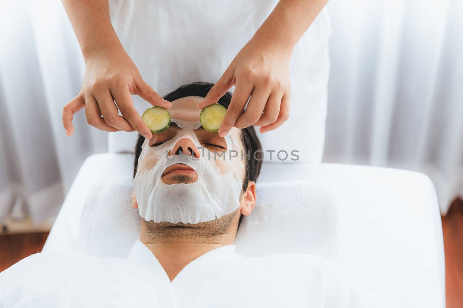 Serene daylight ambiance of spa salon, man customer indulges in rejuvenating with luxurious cucumber facial mask. Facial skincare treatment and beauty care concept. Quiescent