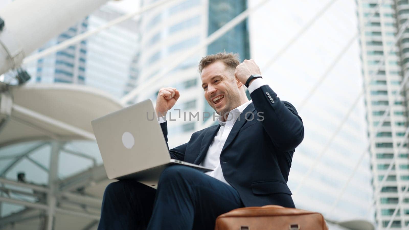 Low angle view of professional business man working on laptop at stairs while celebrate successful project. Caucasian project manager using computer to plan marketing strategy at urban city. Urbane.