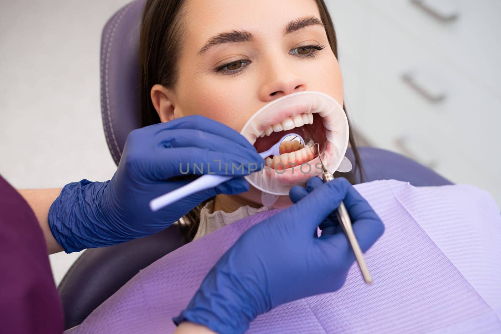 Portrait of young woman in dental clinic. Dentist in rubber gloves doing check up