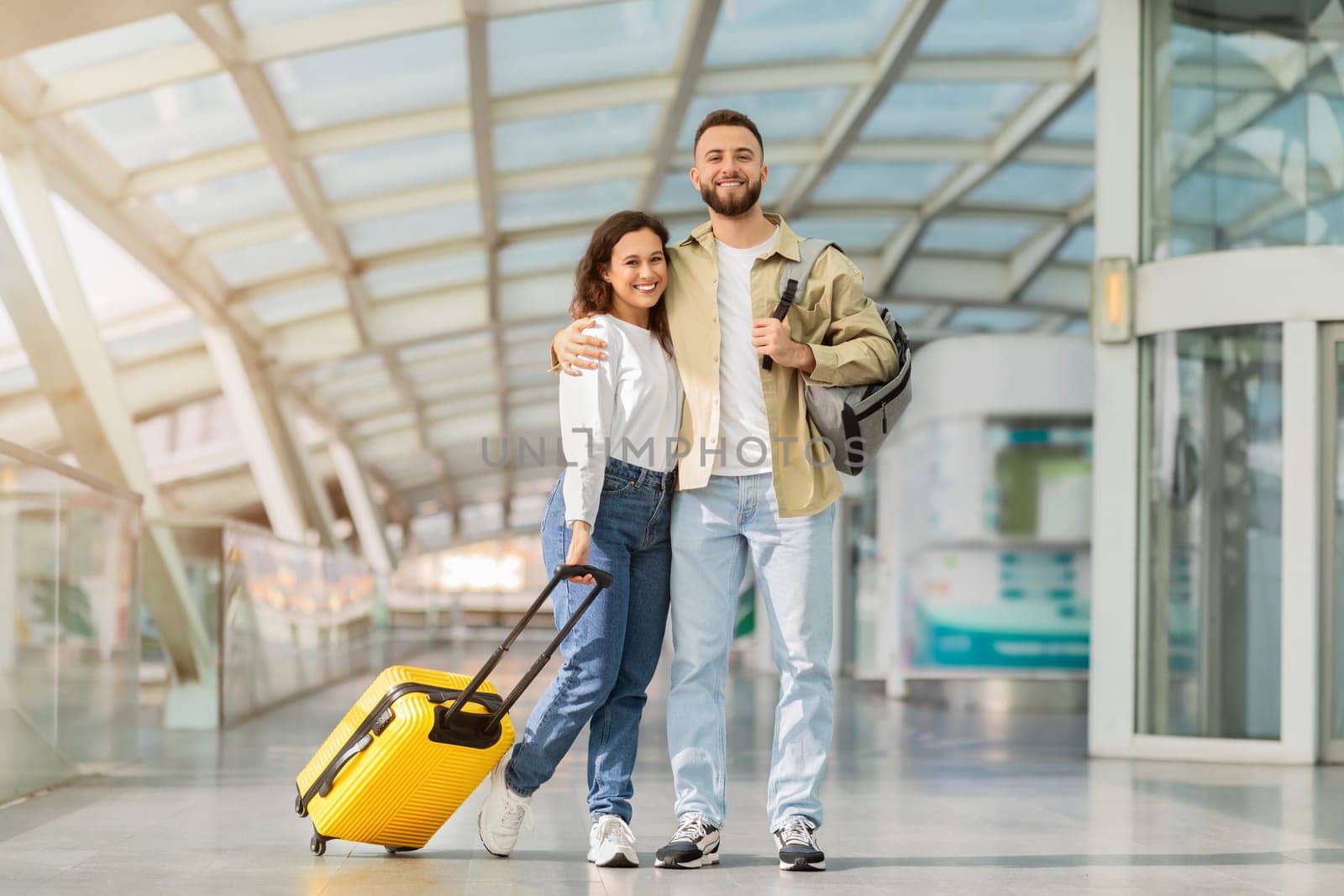 Ready For Trip. Happy Young Couple Posing In Airport Terminal, Cheerful Millennial Man And Woman Standing With Suitcase And Smiling At Camera, Waiting For Flight, Enjoying Travelling Together