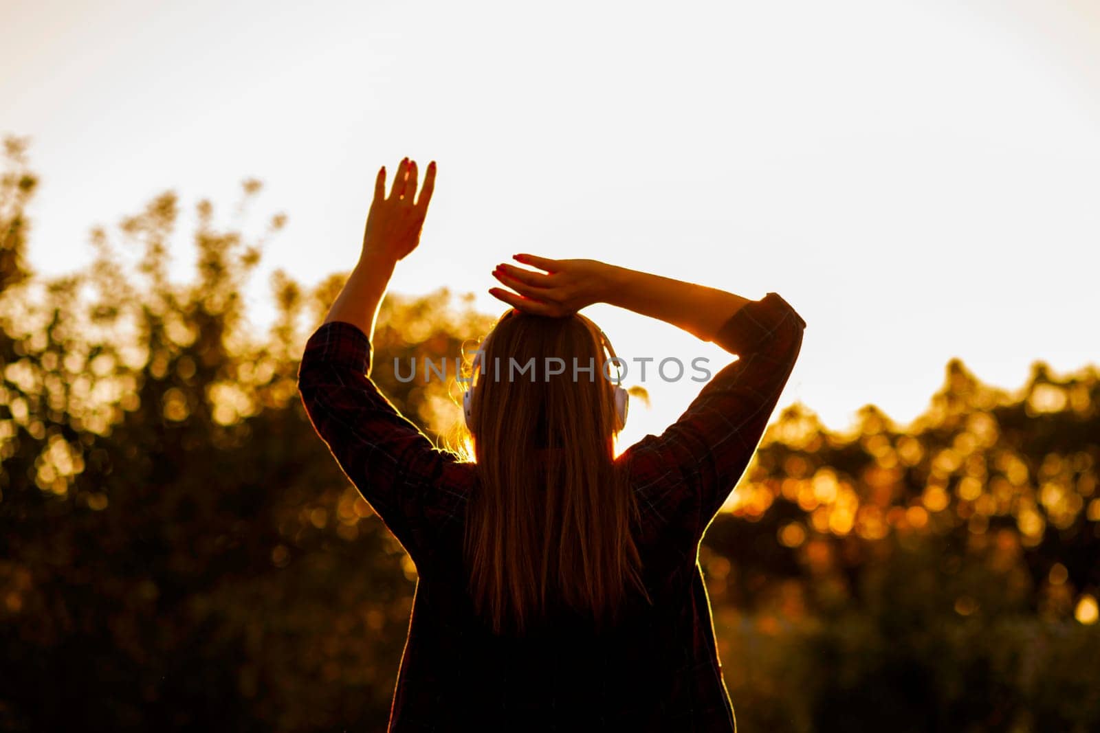 Silhouette of a relaxed woman with headphones enjoying the golden hour of a peaceful sunset.