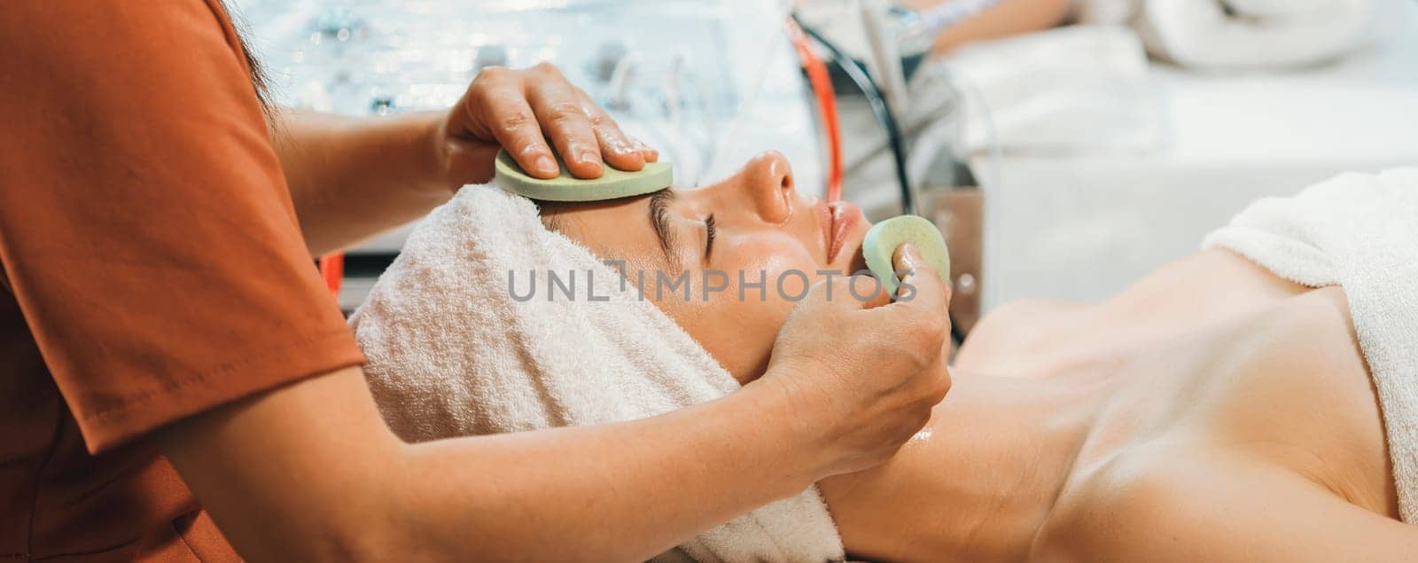 Beautiful young women lie on spa bed while having facial massage from professional doctor. Attractive female with beautiful skin surrounded by electric facial machine. Tranquility.