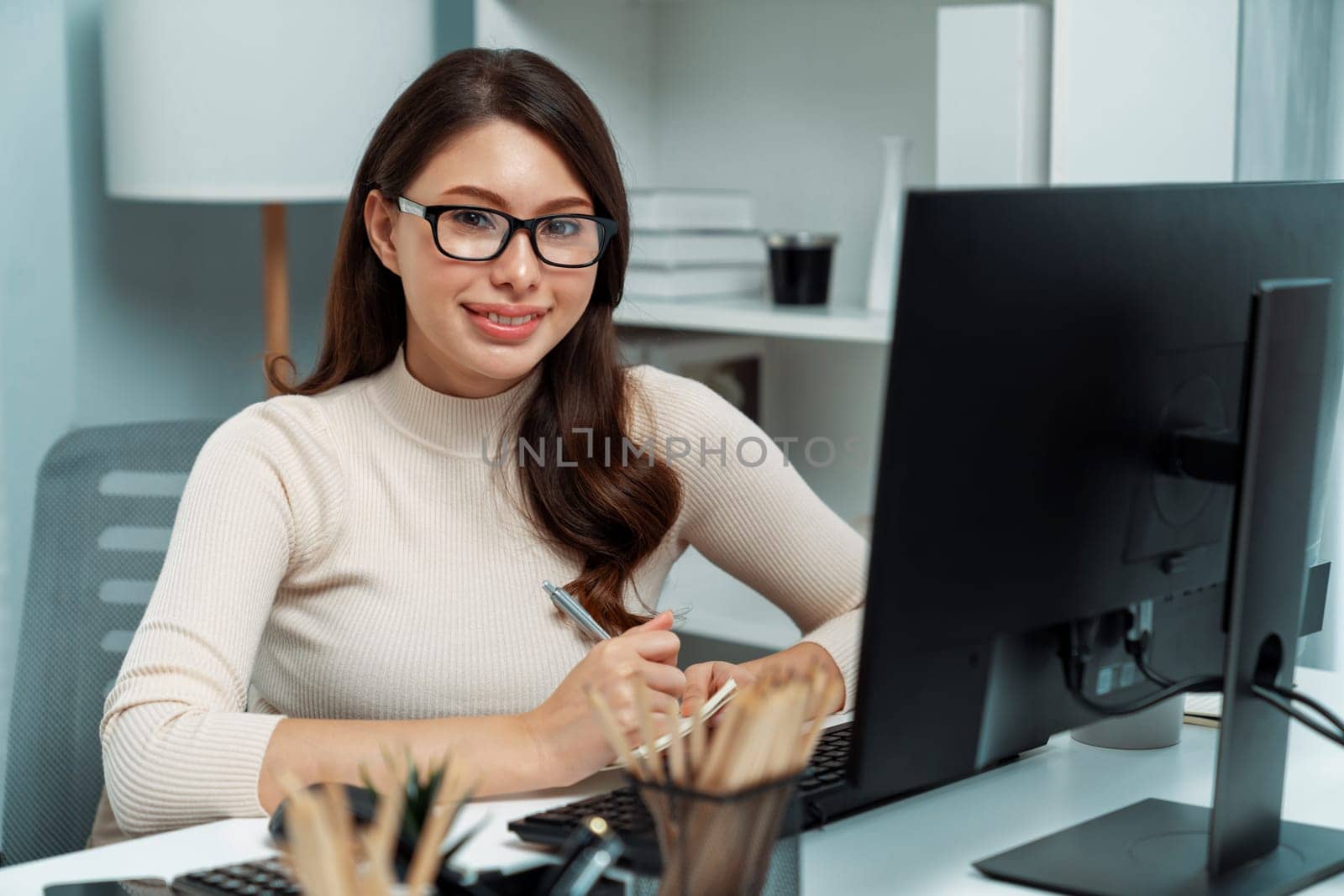 Portrait casual outfit smiling beautiful woman looking camera to pose for business profile while working on desk surrounded pc and stationary theme of positive new generation modern office. Postulate.