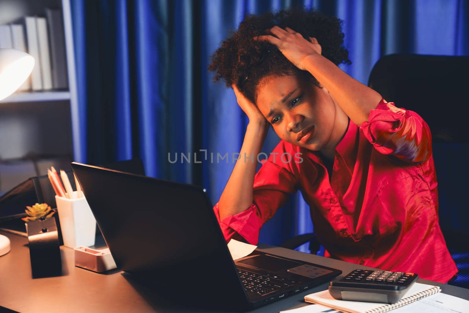 African woman businesswoman, wearing pink shirt having headache with migraine, sitting at computer laptop with leaning position. Concept of work form home with pressure and tension. Tastemaker.