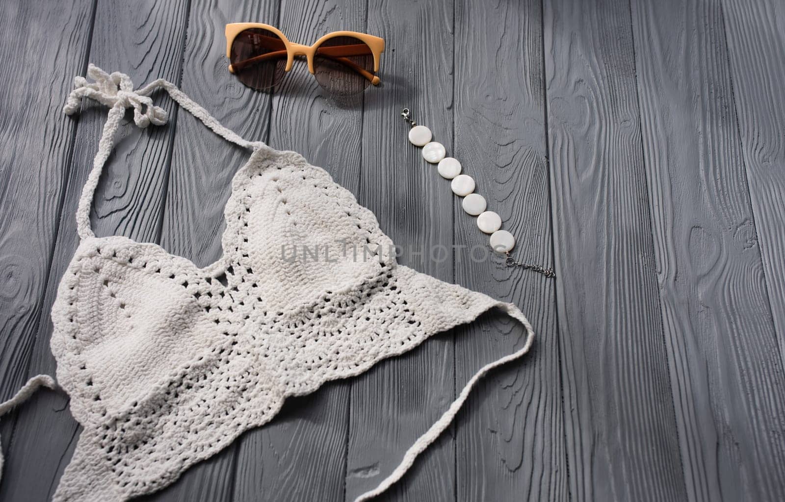 white knitted top woman trending two-piece swimsuit beach swimwear fashion sunglasses. Summer background template mockup space pattern composition sample text. Top view above grey wooden background.