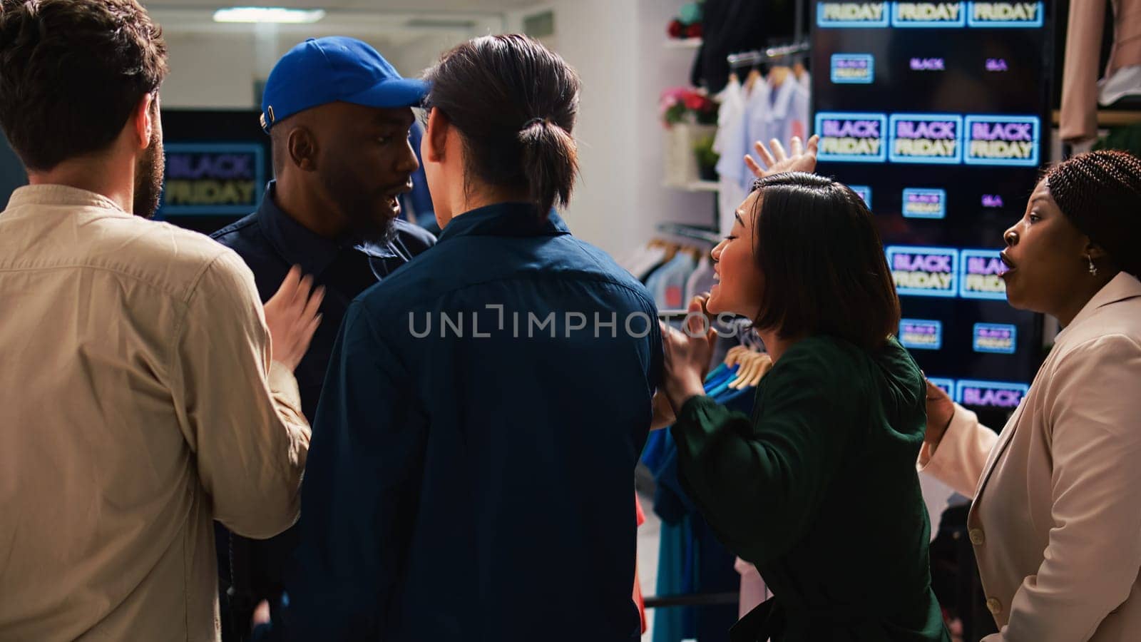 Security officer calms crowd on black friday sales rush, pushing people back and trying to control clothing store entrance. Clients shoppers being impatient, obsessed with cheap prices.