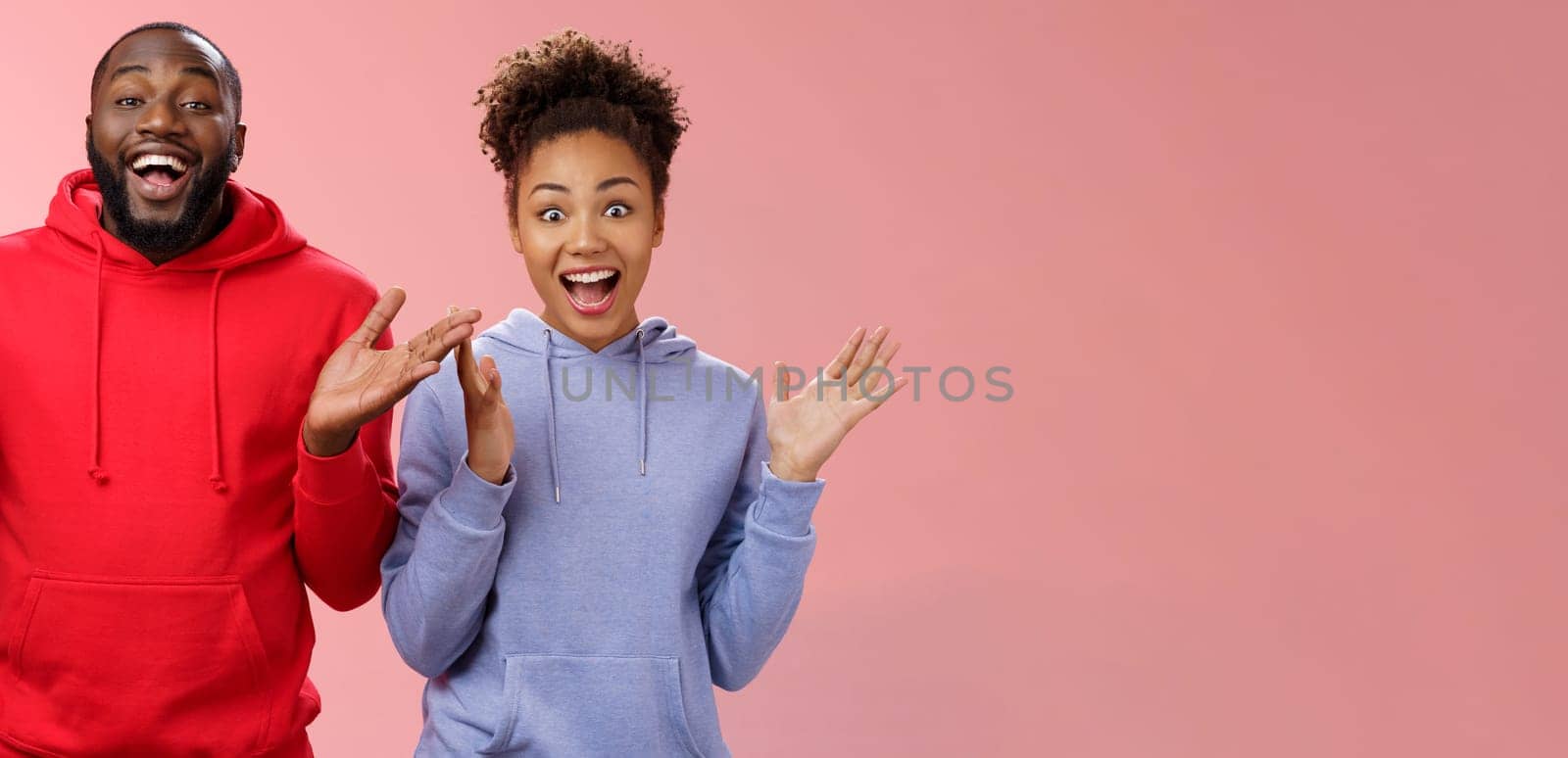 Guys receive nice surprise. Two attractive carefree surprised happy african man woman clapping hands joyfully greeting welcoming guests inviting people joing party standing friendly pink background.