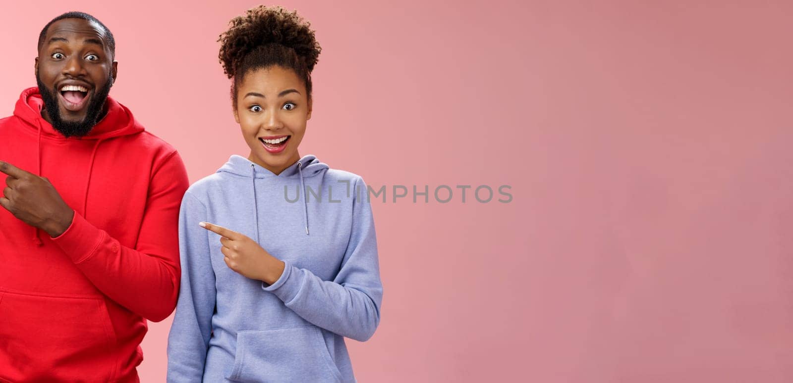 Impressed two best friends african american man woman 25s drop jaw amused visit awesome interesting park pointing left index fingers widen eyes thrilled having fun together, standing pink background by Benzoix