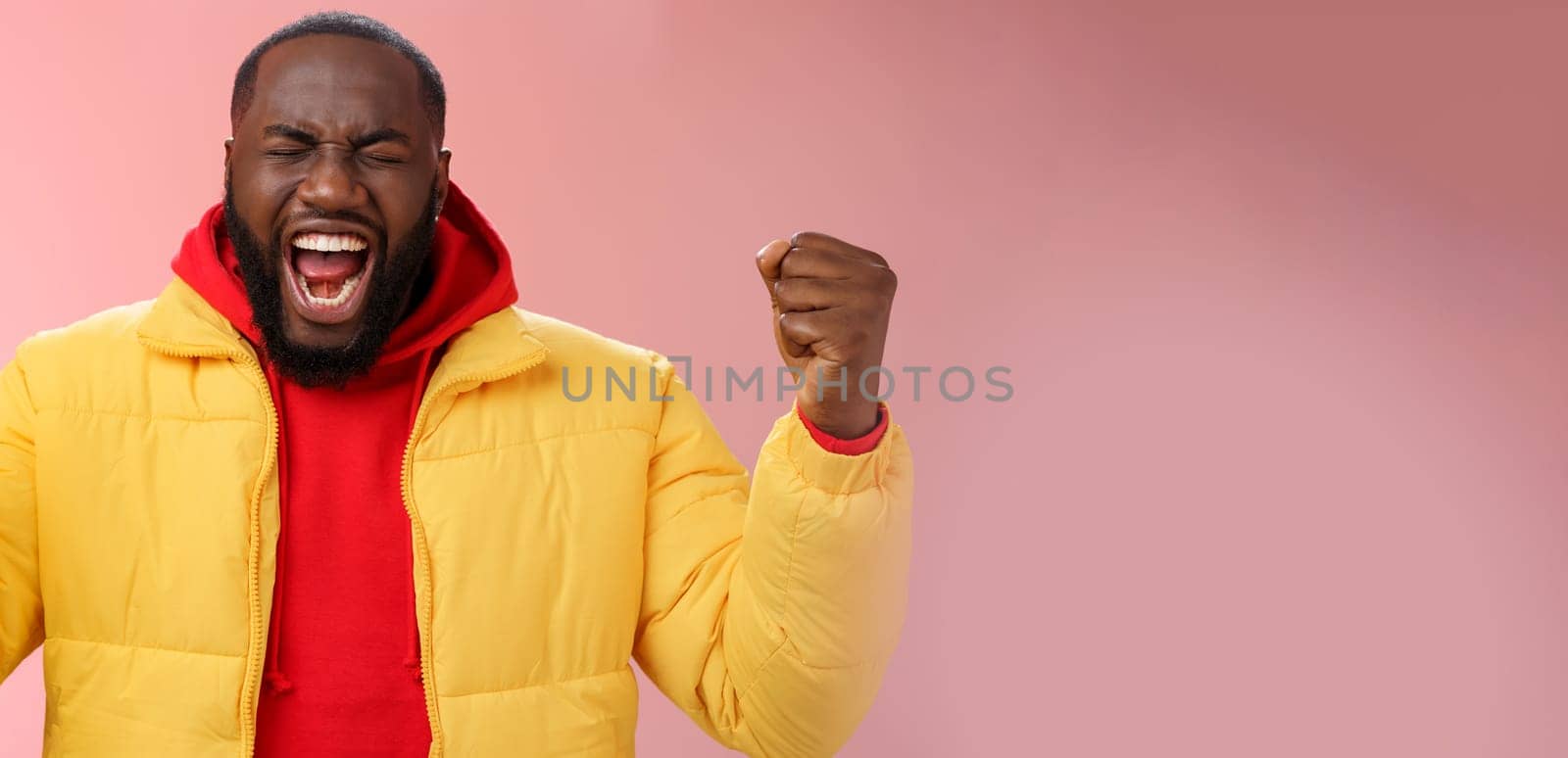 Handsome african-american man encouraging himself put will effort clenched arms yelling close eyes raise hands boost confidence, standing pink background express rage release emotions.