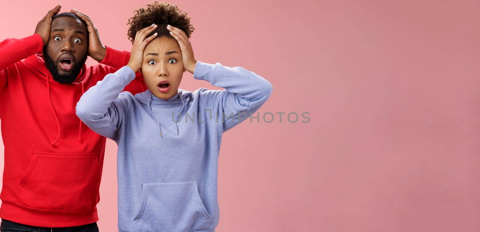 Shocked worried african american couple man woman holding hands head panicking widen eyes stunned receive bad concerning news feel troubled nervous, standing pink background anxious.