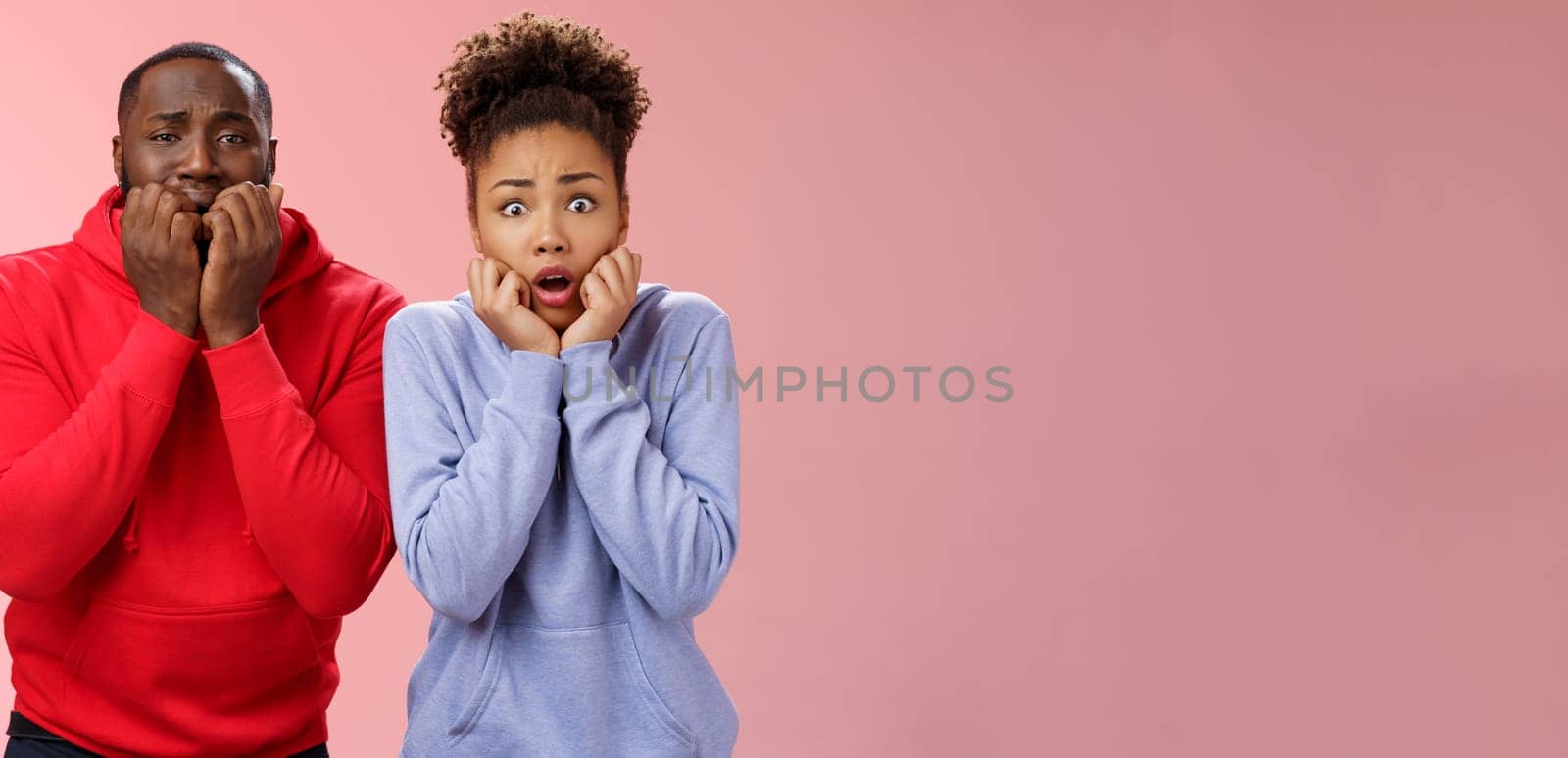 Shocked scared two insecure young african american couple both frightened spiders standing bed terrified freeze from fear holding hands mouth biting fingers shaking horror, pink background by Benzoix