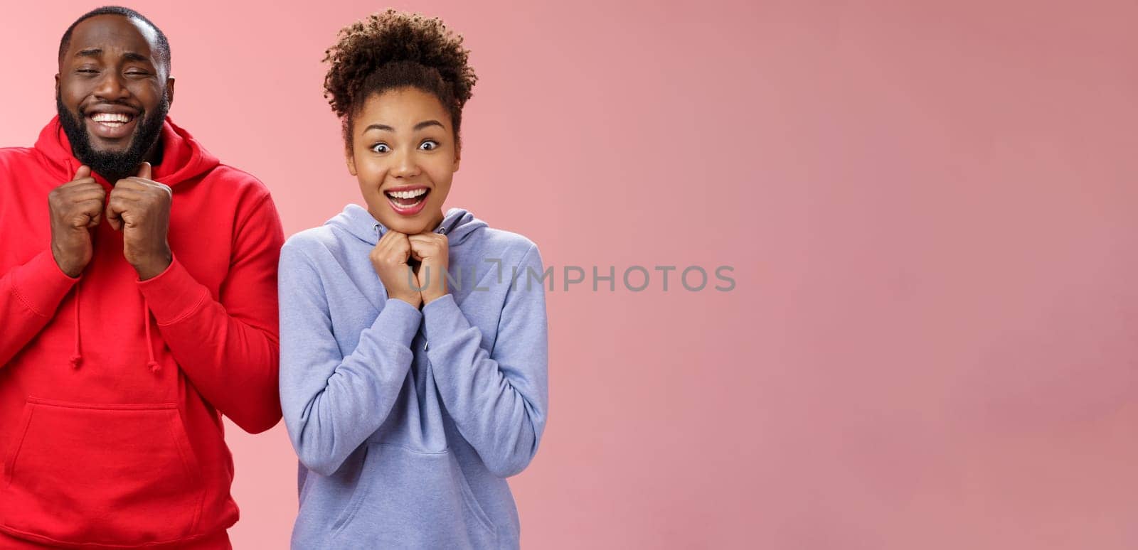 Excited happy girlfriend boyfriend smiling broadly nervously clenching fists pressed chest looking camera thrilled anticipate good news trying luck playing lottery together, standing pink background by Benzoix