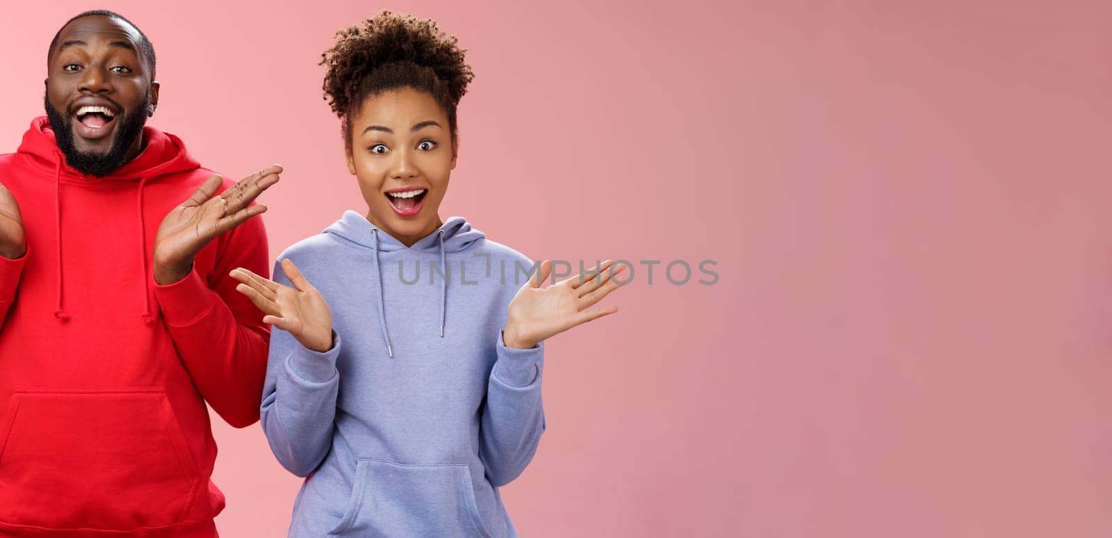 Impressed happy thrilled young pair african man woman relationship clapping palms joyfully surprised wide eyes joyfully greeting friends inviting come in hospitable, standing pink background.