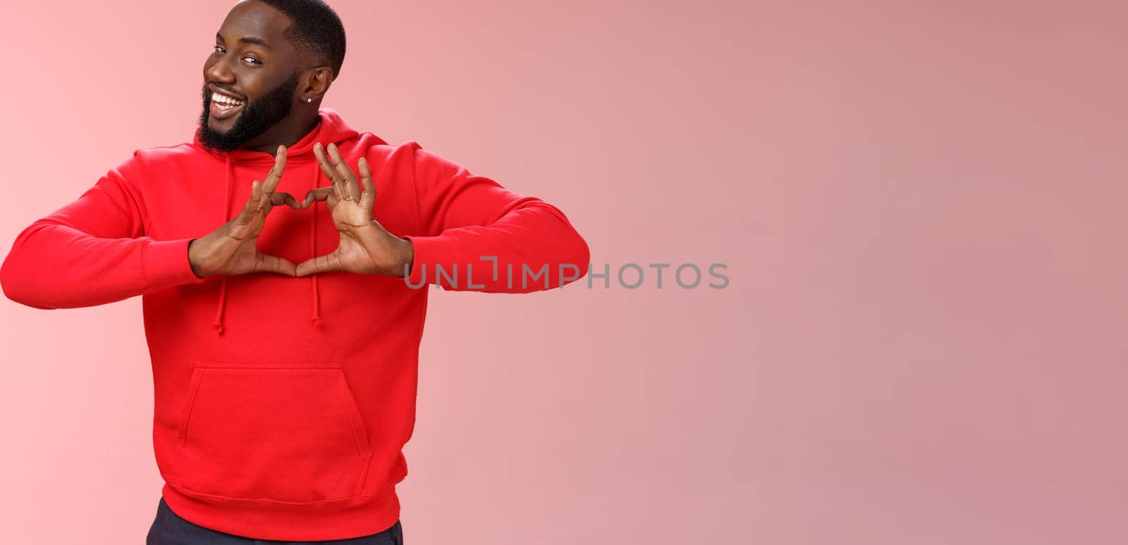 Someone love ya. Portrait enthusiastic creative cute black boyfriend wearing red hoodie show heart sign smiling broadly confessing love sympathy look passionate, express romance pink background.