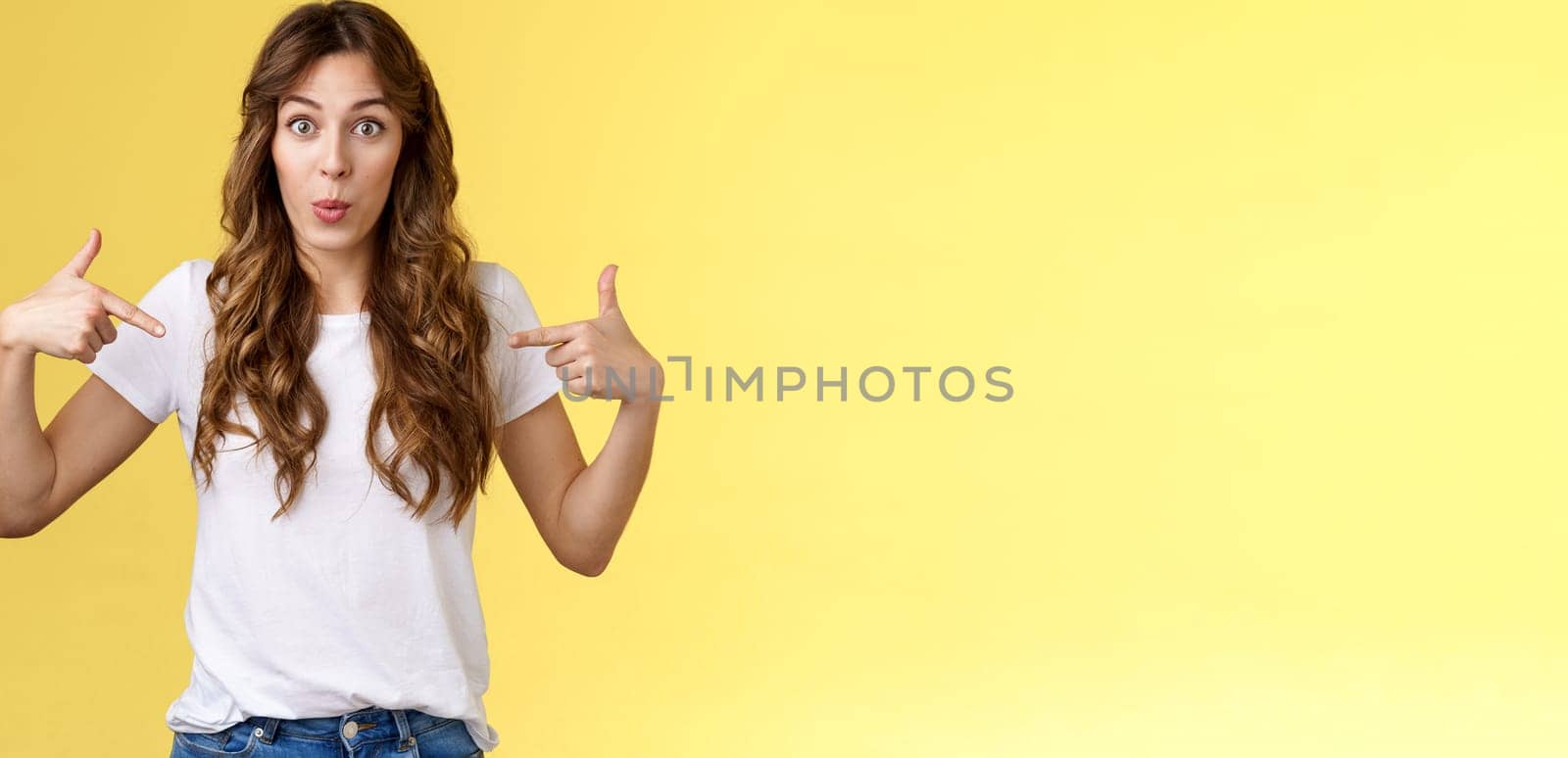 Wow just look. Impressed surprised cute wondered european girl pointing fingers center copy space white t-shirt folding lips amused astonished awesome promo great chance gaze you camera.