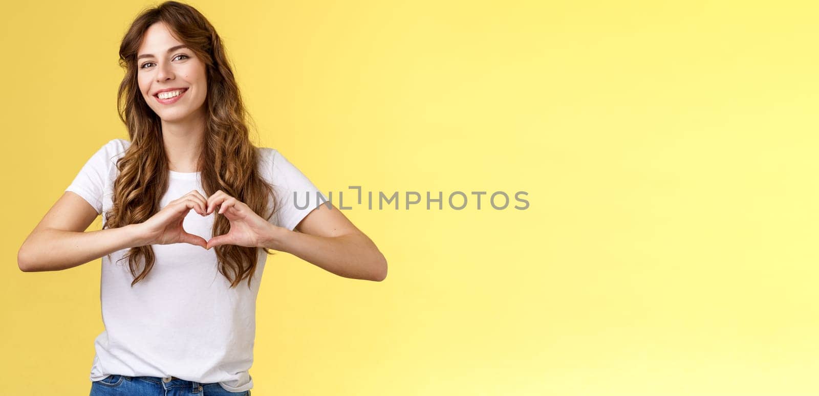 Carefree tender attractive woman curly long hairstyle show heart sign near chest express love like summer memories smiling broadly tilt head joyfully confess romantic feelings cherish friendship. Lifestyle.