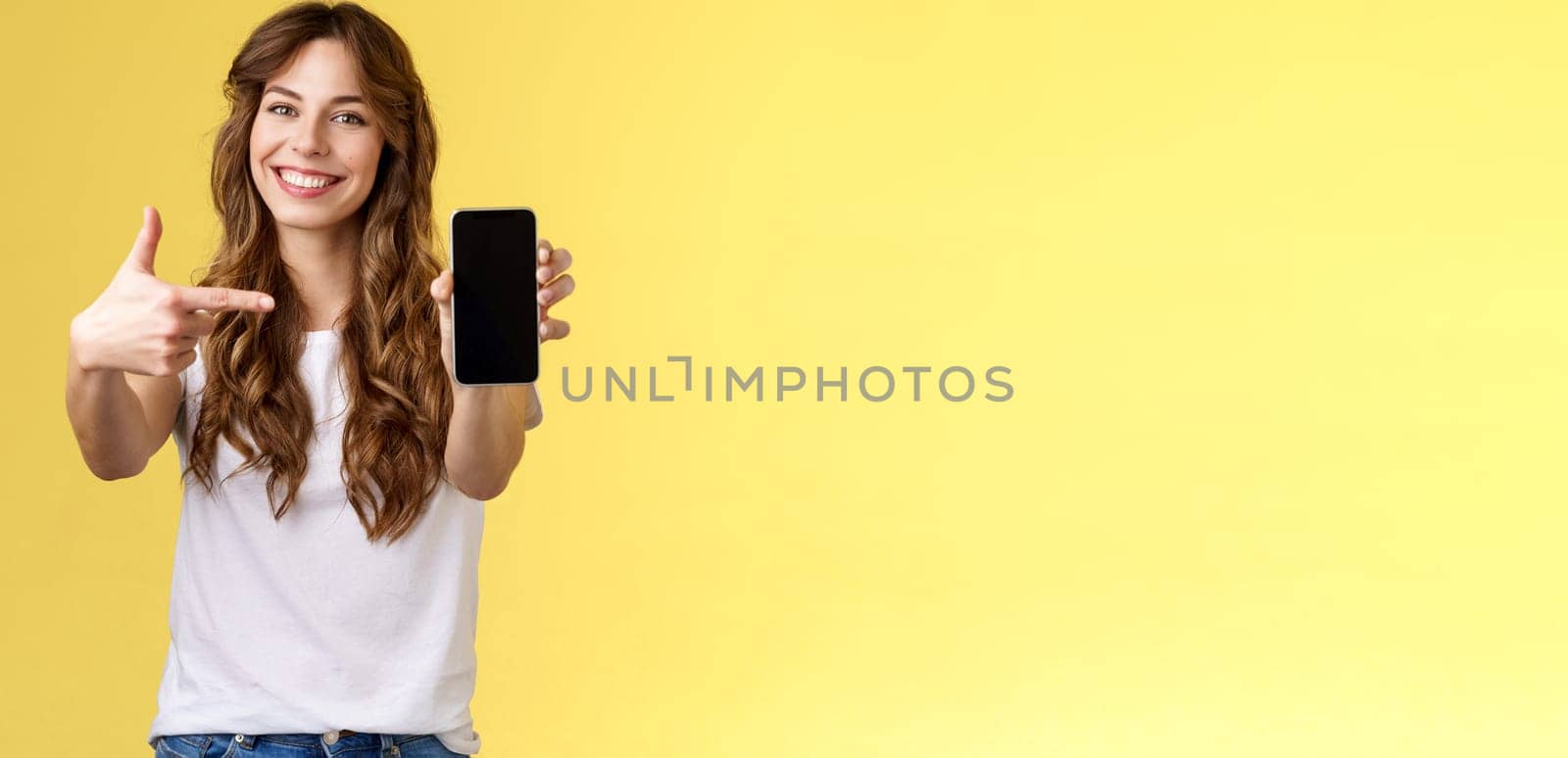 Upbeat confident good-looking female showing photo smartphone display hold mobile phone extended arm camera pointing index finger cellphone screen smiling delighted promote app internet application by Benzoix