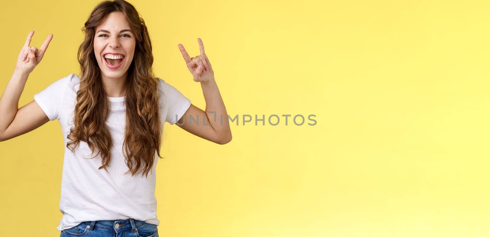Girl having fun excellent awesome concert enjoy live music show rock-n-roll heavy metal gesture yelling upbeat happy attend cool festival party smiling broadly show tongue daring yellow background. Lifestyle.