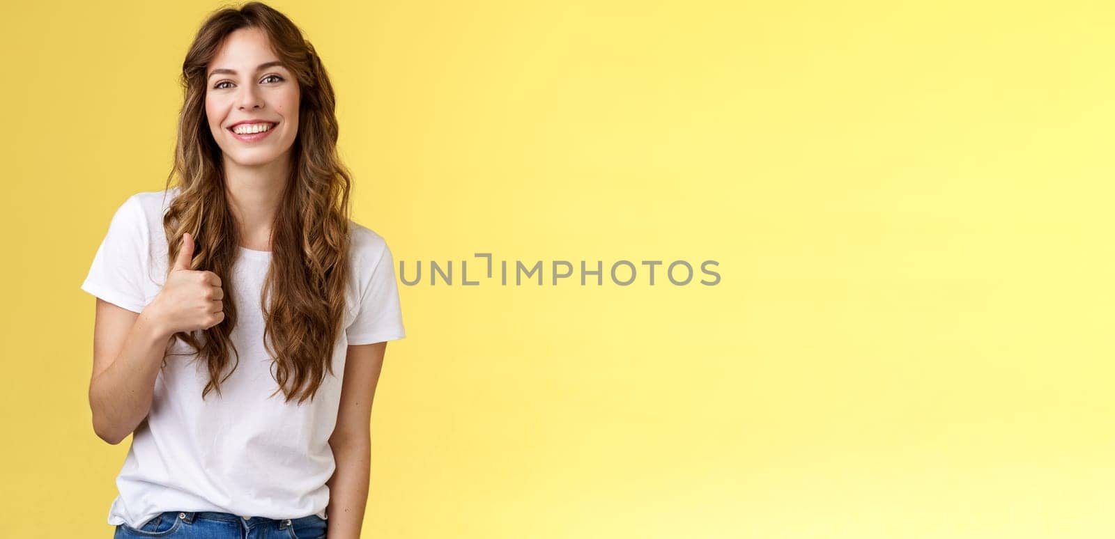 Girl thinks you done great job. Smiling cheerful good-looking woman long curly haircut approve perfect choice give thumb up agree like your style grinning support excellent idea yellow background.